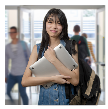 Teenage girl holding a laptop in her arms in her high school hallway as students walk past