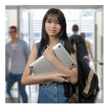 Teenage girl holding a laptop in her arms in her high school hallway as students walk past