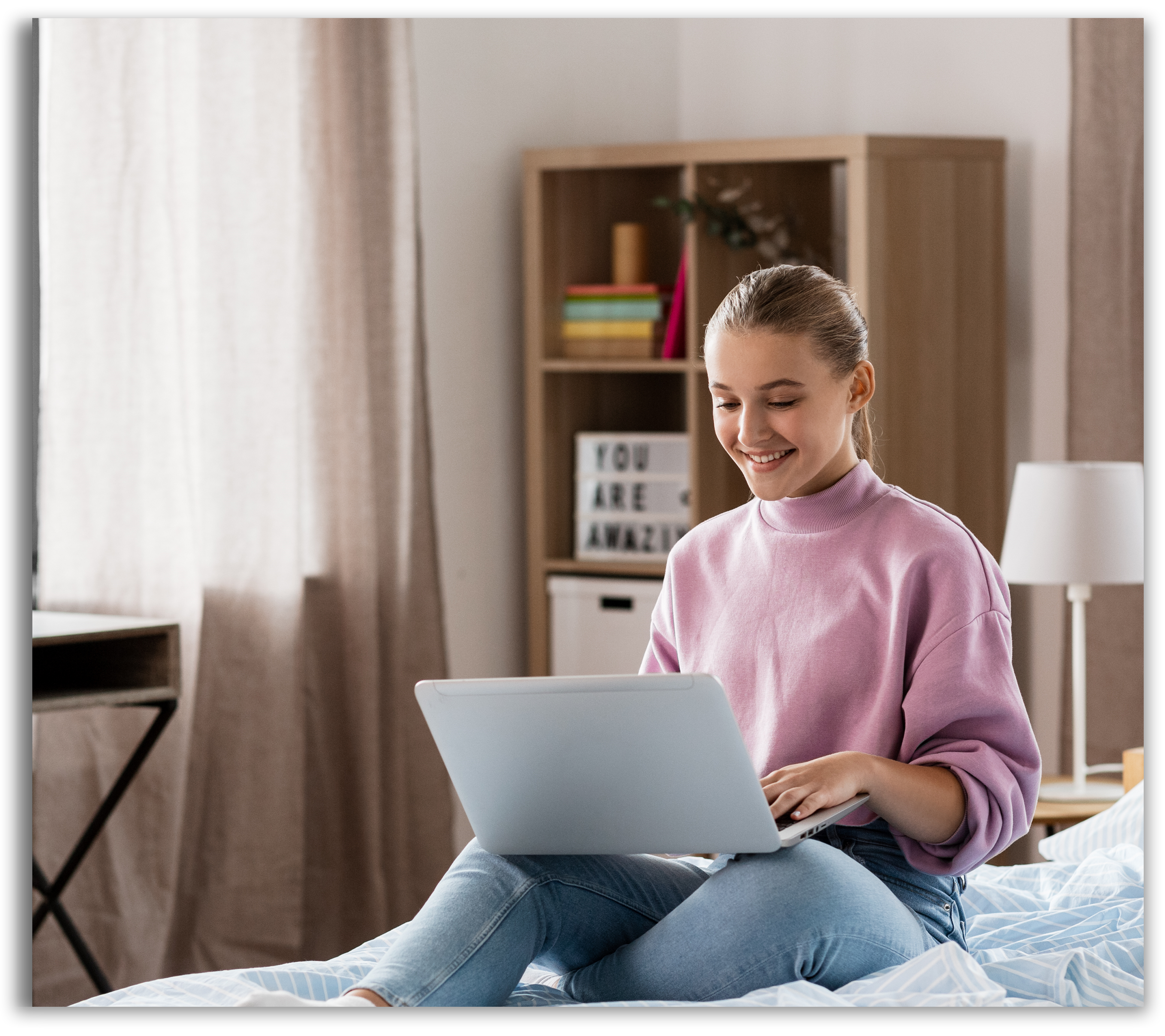 Girl doing homework on laptop while sitting on her bed