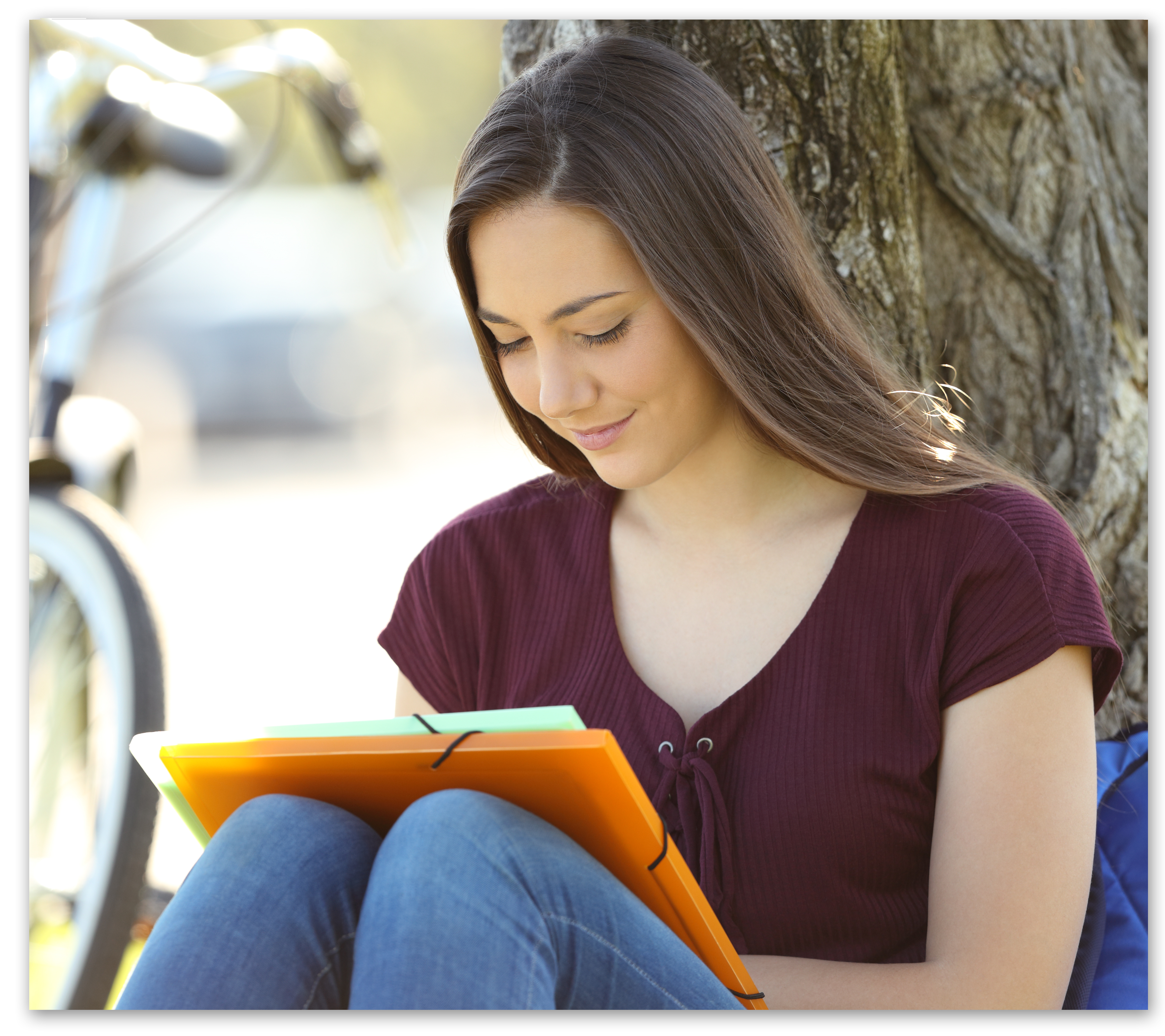 Teenage girl sitting in front of tree doing homework