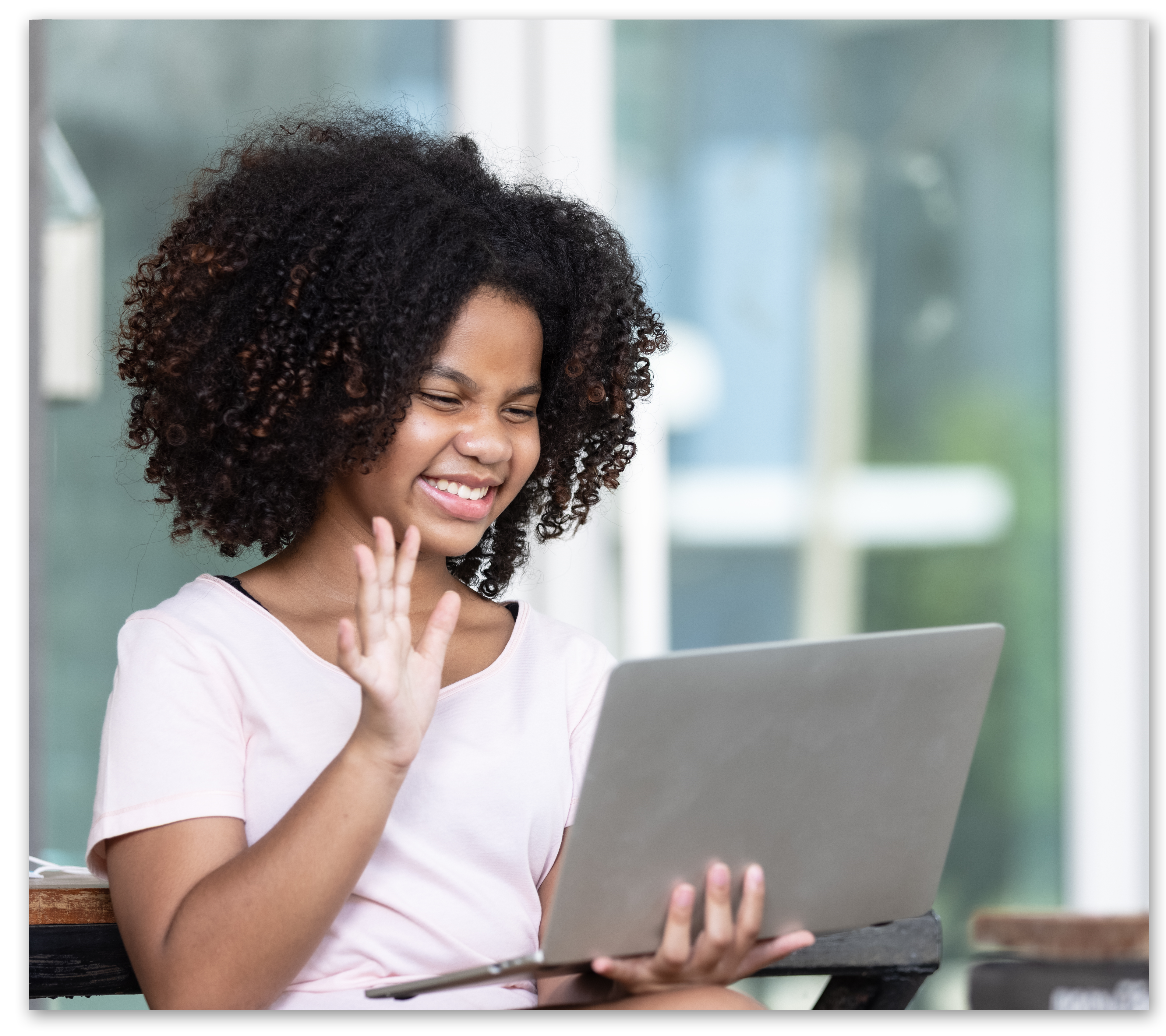 Girl smiling and waving to webcam on laptop