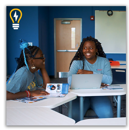 Two girls work together in a hybrid classroom using laptops