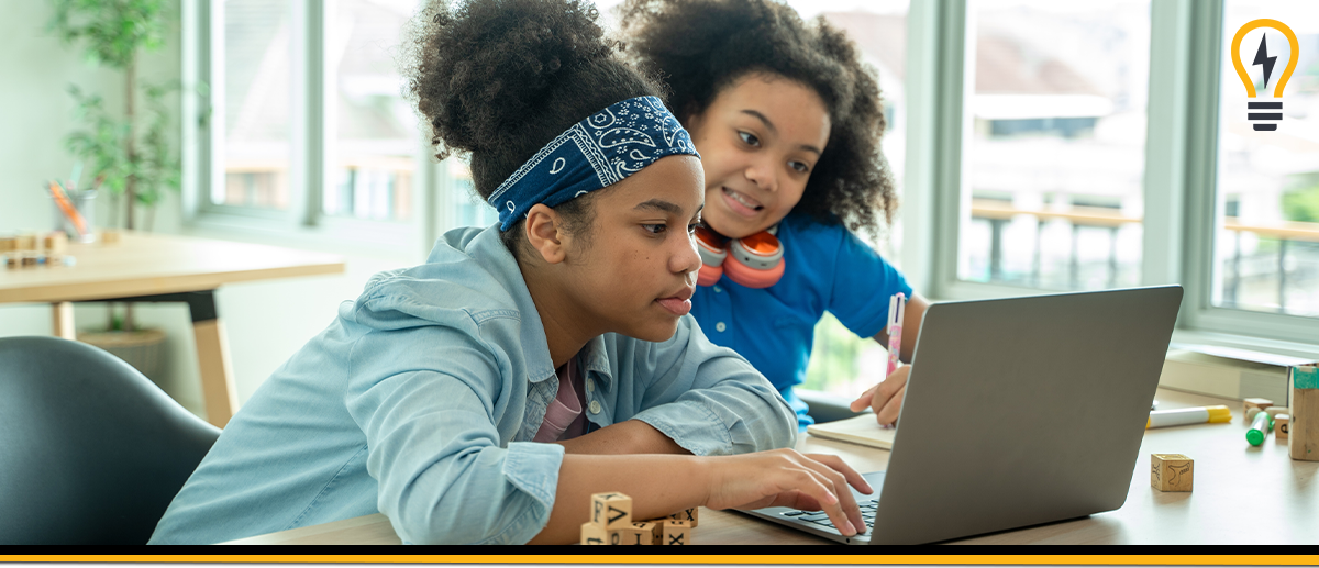 Two girls working in a hybrid classroom, looking at a laptop