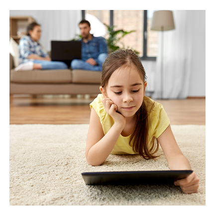 Student on a tablet at home with parents behind her on a couch